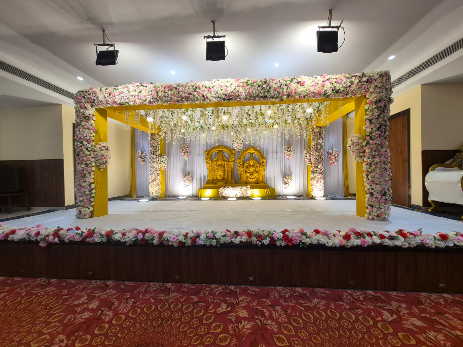 Wedding mandap with pink and white floral canopy and golden deity idols