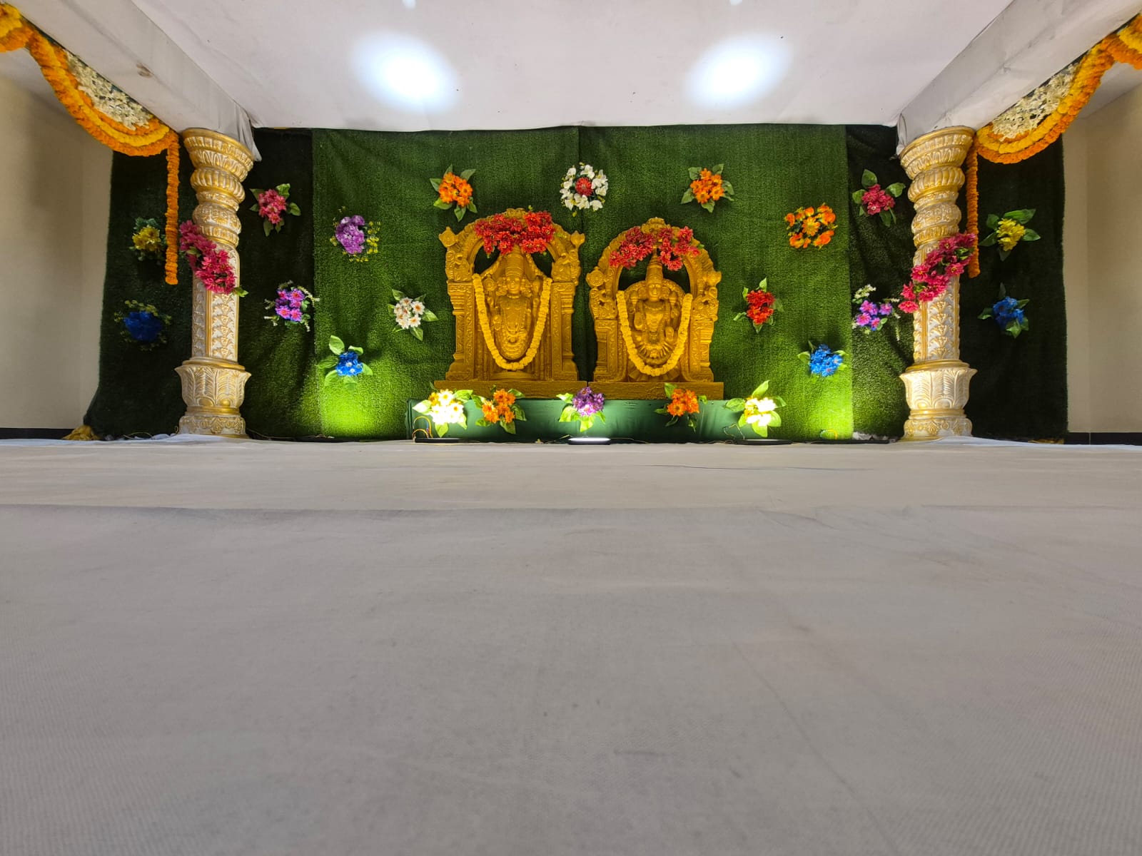 Wedding stage with golden deity idols, green backdrop and carved pillars