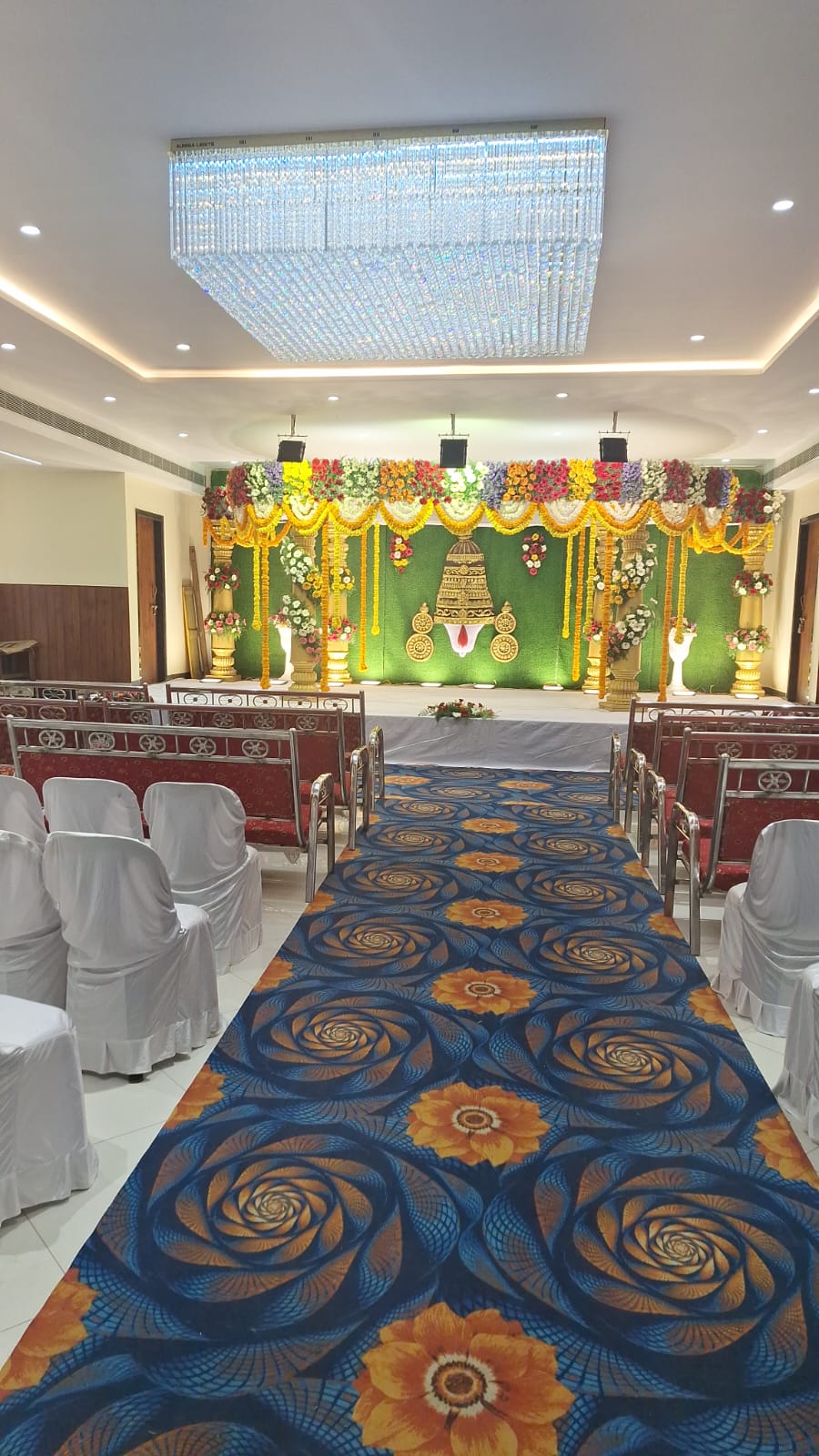 Wedding mandap with green backdrop, marigold garlands and decorated aisle carpet
